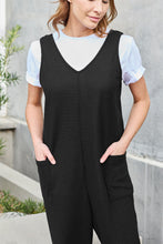 Close-up front view photo of model in black Caeloura Jumpsuit highlighting the convenient pocket detailing, V-neck, and quality waffle knit fabric.