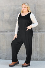 Side profile of black Caeloura Jumpsuit, highlighting pockets and flowing straight-leg fit styled with brown boots.
