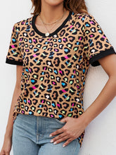 Model wearing a camel leopard print short sleeve tee, walking a dog in the park, styled with light-wash denim and a crossbody bag.