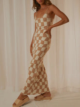 Side view of a model wearing the Camel Luxnometry Maxi Sweater Dress, highlighting the sleek drape and bold geometric pattern in a luxurious mansion hallway.