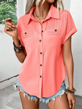 Model wearing a coral pleated collared neck short sleeve blouse with button-up front, paired with light denim jeans, styled for a casual day out.