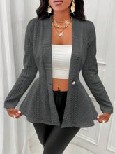 A model posing in a dark gray One Button Textured Peplum Cardigan paired with a white top, black pants, jewelry, and heels.
