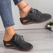 A model showcasing the sides of a pair of the dark grey Lace-Up Round Toe Wedge Sandals and a gold anklet and blue jeans.