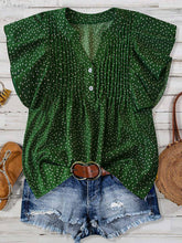 Front view of EverDot Flutter Top in dark green polka dot with flutter sleeves paired with earrings, belt, brown sandals, and straw handbag in a flat lay photo.