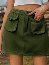 Close-up front view of Denovelle dark green denim mini skirt with model’s hand in front flap pocket
