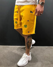 Side walking view of men’s yellow shorts with animal and letter embroidery.