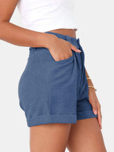 Close up photo of female model highlighting the pocket detailing of the Dusty Blue Metropolitan Maven High-Waist Shorts paired with a white tank top and jewelry.