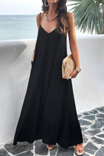 a model posing on a balcony wearing a black Backless Maxi Cami Dress with Pockets  paired with jewelry, a woven handbag, and clear heels