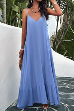 a model posing on a balcony wearing a sky blue Backless Maxi Cami Dress with Pockets  paired with jewelry, a woven handbag, and clear heels