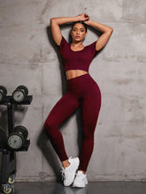 Model in Burgundy EroVital Fusion Active Set leaning against gym wall with weights.