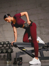 Woman lifting dumbbells on bench wearing Burgundy EroVital Fusion Active Set.