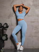 Model in Light Blue EroVital Fusion Active Set leaning on gym wall beside weights.