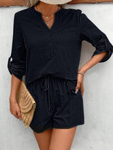 Woman standing against a cottage wall posing in black Everyday Escape Notched Sleeve Short Set styled with accessories for a laid back casual look.