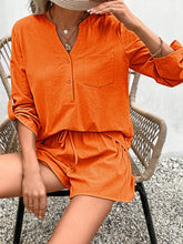 Model wearing bold orange Everyday Escape Lounge Set sitting in a chair by the poolside with sunglasses and a straw hat.