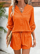 Model in vibrant orange Everyday Escape Lounge Set standing with straw hat and straw handbag by the beachside.