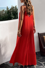 A model showcasing the back of a deep red Backless Maxi Cami Dress with Pockets paired with jewelry and clear heels posing on an Oceanview balcony 
