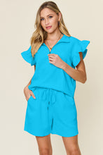 Model lounging in sky blue Facts Only Fit Set with flat sandals, holding iced coffee.