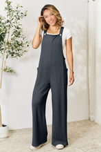 Model styled in Cloudy Blue Cyrella Muse Overalls with a tucked-in tee and sneakers.
