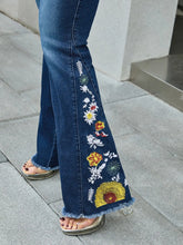 Close-up detail of floral embroidery on side pant leg of women’s dark blue flare jeans.