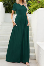 Model posing on a white staircase in the forest green Blissurella Maxi Tee Dress with layered jewelry and tan heels for a casual garden party.