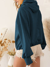 A model showcasing the back of a  french blue color Nuvella Zip-Up Dropped Shoulder Hoodie paired with distressed tan denim shorts.