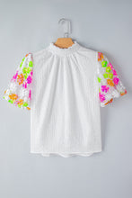 Front view of LustruBloom Blouse showcasing sequin floral half sleeves and ruched mock neckline, on a hanger.