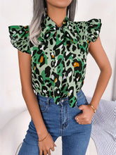 Model styled in a green leopard print tie-neck blouse with cap sleeves, standing confidently in tailored trousers and gold jewelry.