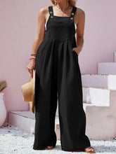 Side profile of model in black overalls styled with heeled sandals and hoop earrings.