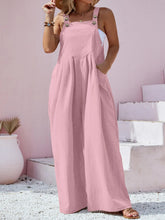 Model in dusty pink Harmonique overalls on a sunny café patio paired with a straw tote and gold jewelry.