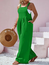 Model in green Harmonique overalls at a picnic paired with sandals and a sunhat.