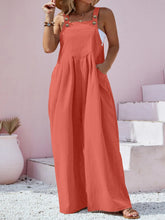 Side profile of orange overalls styled with strappy heels and stacked bangles.
