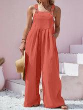 Model in orange Harmonique overalls enjoying a sunset beach stroll with sandals and a woven bag.