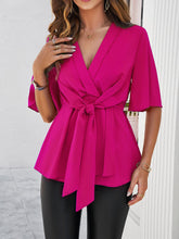 Model wearing a hot pink tied front peplum blouse, styled with distressed jeans and heels for a chic, casual daytime look.