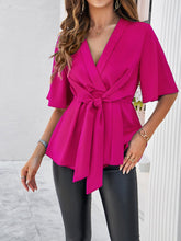Model wearing the hot pink tied front peplum blouse at a beachside resort, paired with wide-leg pants and sandals for an effortlessly chic vacation look.