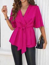Model standing by a cozy cottage in a hot pink tied front peplum blouse and denim shorts, perfect for a relaxed weekend getaway vibe.