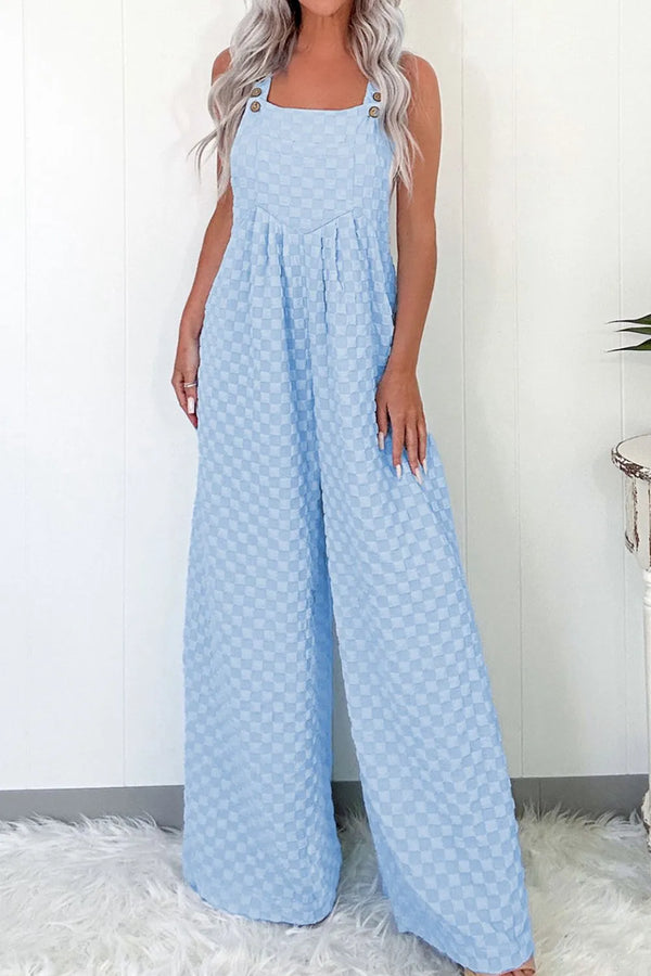 Model in light blue checkered wide-leg overalls relaxing at an outdoor café with iced coffee on a pursian white fur carpet.