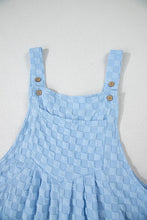 Close-up of top half front of checkered overalls showing buttons, chest, and strap details.