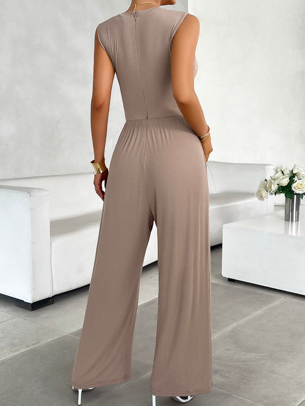 A model showcasing the back of a Mocha color Devine Round Neck Sleeveless Wide Leg Jumpsuit paired with gold jewelry and white heels
