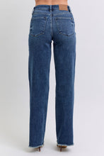 A female posing from the back wearing dark blue Judy Blue Full Size Raw Hem Mid Rise Denim Jeans paired with a red blouse, jewelry, and red pointed-toe heels.