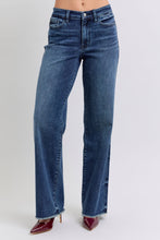 A female posing from the front wearing dark blue Judy Blue Full Size Raw Hem Mid Rise Denim Jeans paired with a red blouse, jewelry, and red pointed-toe heels.