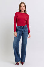 A female posing from the front wearing dark blue Judy Blue Full Size Raw Hem Mid Rise Denim Jeans paired with a red blouse, jewelry, and red pointed-toe heels.