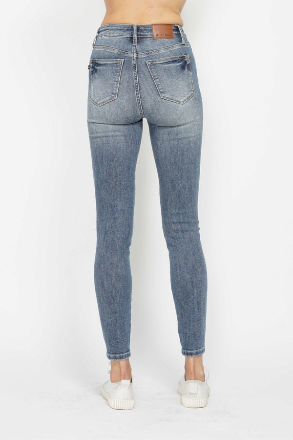 A female posing from the back wearing medium blue Judy Blue Full Size Tummy Control Contrast Washed Skinny Jeans paired with a plaid button-up shirt, jewelry, and white sneakers.