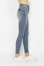 A female posing from the side wearing medium blue Judy Blue Full Size Tummy Control Contrast Stonewashed Skinny Jeans paired with a plaid button-up shirt, jewelry, and white sneakers.
