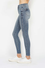 A female posing from the side wearing medium blue Judy Blue Full Size Tummy Control Contrast Stonewashed Skinny Jeans paired with a plaid button-up shirt, jewelry, and white sneakers.