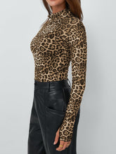 Side profile of model in leopard print mock neck top with thumb-holes, styled with hoop earrings and dark jeans.