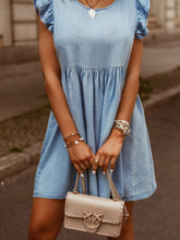 Model in light blue Sylvenza Denim Dress styled with tan and gold handbag and accessories standing on urban city street.