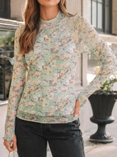 Side profile of model in light green print mock neck top with thumb holster, styled with hoop earrings and dark jeans.