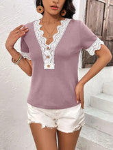 Model wearing a lilac Lace Detail V-Neck Short Sleeve T-Shirt with wavy lace trim neckline and sleeves, styled with light-wash jeans in a sunny outdoor setting.