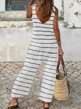 Model showcasing the back view of the Lunalvia Striped Round Neck Wide Leg Jumpsuit while walking toward a charming coastal cottage, paired with flat sandals and a tan straw handbag, highlighting the jumpsuit’s relaxed, breezy fit from behind.