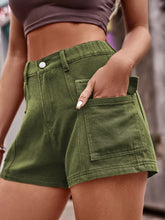 Side view of a woman in a graphic tee and matcha green Joyful Journey Denim shorts skateboarding in a park.